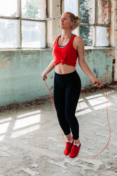 Athletic fit girl rope jumping. Fitness training, healthy lifestyle. Indoors shot in an old building - Foto, afbeelding