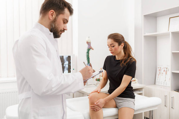 Male doctor examining female patient suffering from knee pain. Medical exam. Chiropractic, osteopathy, post traumatic rehabilitation, sport physical therapy. Alternative medicine, pain relief concept - Foto, Bild