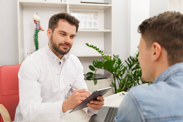 Doctor and patient in medical office. Therapist talking to patient in office, taking notes, writing prescription. Consultation in clinic. Healthcare and medicine concept - Foto, Bild