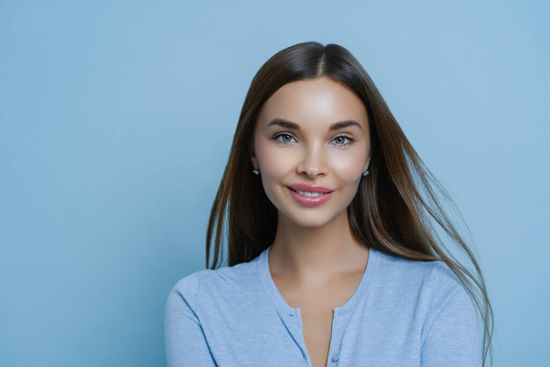 Headshot of tender girlfriend with pleasant appearance, smiles tenderly, arranges spa salon relaxation weekend, satisfied after cosmetic procedures, has healthy fresh skin, isolated on blue background - Photo, Image