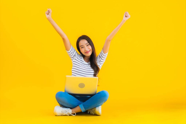 Portret mooie jonge aziatische vrouw gebruik laptop of notebook voor werk en studie op geel geïsoleerde achtergrond - Foto, afbeelding
