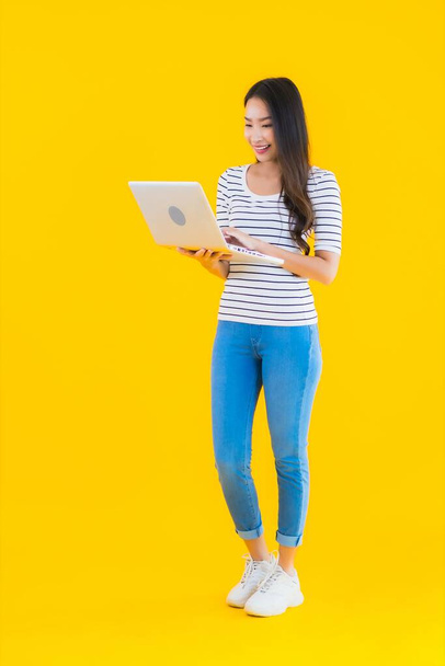 Портрет красива молода азіатка використовує ноутбук або блокнот для роботи та навчання на жовтому ізольованому фоні
 - Фото, зображення