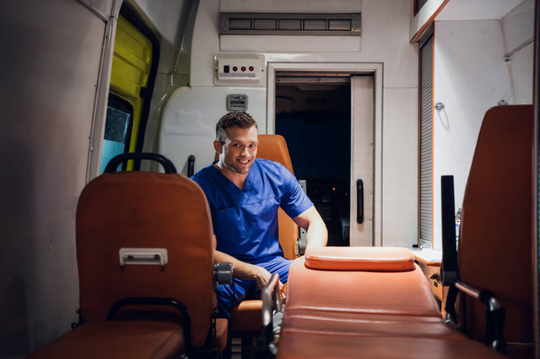Man in een medisch uniform zittend in de ambulance en lachend - Foto, afbeelding