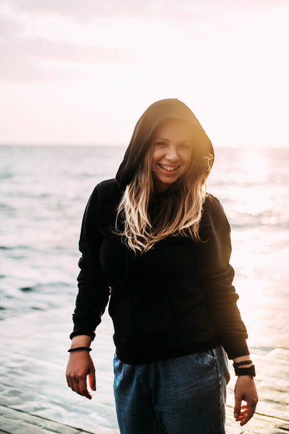  Blurred Young girl stands in a black sweater and jeans with her back to the sun at dawn and smiles. Sun glare in the background. Happy morning. Inspiration, enjoyment - 写真・画像