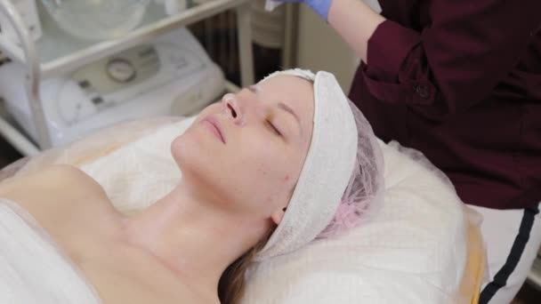 Ammattimainen kosmetologi pesee naamion pois naisen kasvoilta. - Materiaali, video