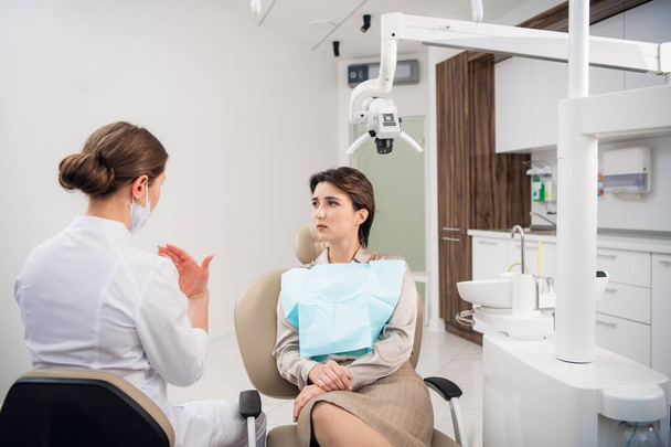 Μια νεαρή γυναίκα οδοντίατρος συμβουλεύεται τον ασθενή της στην κλινική. - Φωτογραφία, εικόνα