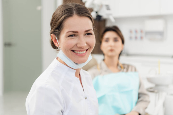 Muotokuva hymyilevä hammaslääkäri toimistossaan, jossa potilas
 - Valokuva, kuva