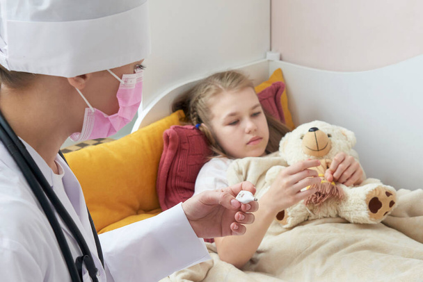 Doktor drží teploměr a kontrolu nemocné holčičky.Nemocná holčička na posteli s horečkou měření teploty - Fotografie, Obrázek