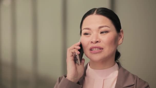 Asian businesswoman talking on the phone on the street. A woman businesswoman in a business suit stands against the backdrop of a business office center. Business concept. Prores 422 - Кадры, видео