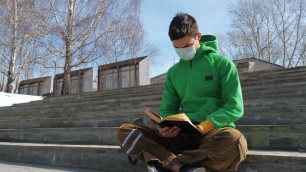 Young man reading book on street during epidemic - Záběry, video