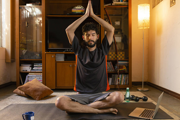 Een jonge Spaanse man die thuis yoga beoefent. Home yoga concept. - Foto, afbeelding