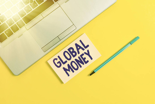 Handschrift tekst schrijven Global Money. Concept betekent Internationale financiën Wereldmunt Wereldwijd doorzocht Trendy zilveren open laptop vierkant plakkerige notitieblok marker gekleurde achtergrond. - Foto, afbeelding
