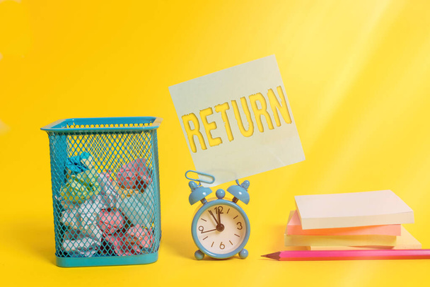Writing note showing Return. Business photo showcasing come or go back to a place or an individual Give money you took before Alarm clock pencil note paper balls container pads colored background. - Photo, Image
