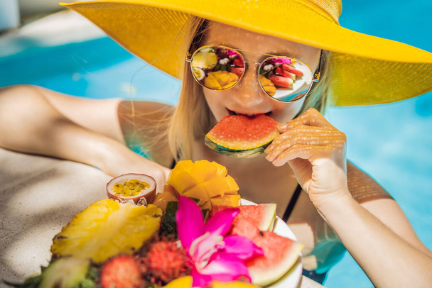 Young woman relaxing and eating fruit plate by the hotel pool. Exotic summer diet. Photo of legs with healthy food by the poolside, top view from above. Tropical beach lifestyle - Foto, Imagem