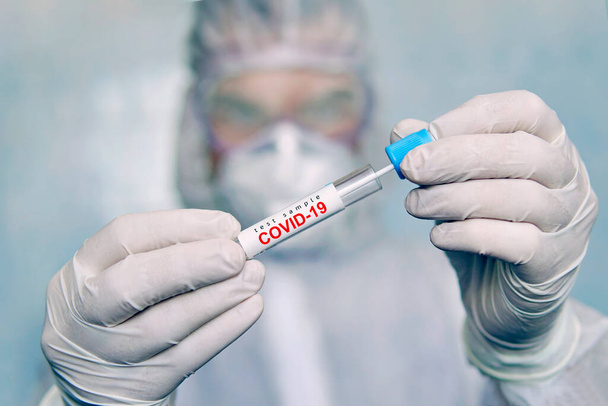 COVID-19. Coronavirus minta COVID-19. tampon koronavírus teszt. Járványkitörés. egy vegyi védőruhás férfi kémcsövet tart elemzésre.. - Fotó, kép