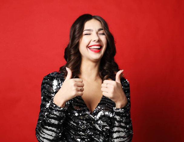 Portrait of a pretty brunette woman in evening dress showing okay sign over red background - Foto, immagini