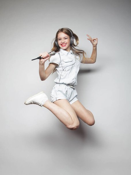 young blond happy woman with microphone jumping and singing - Foto, Imagem