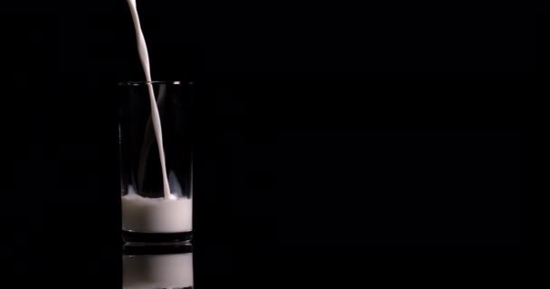 close-up γάλα ρίχνει σε ένα ποτήρι σε μαύρο φόντο σε αργή κίνηση - Πλάνα, βίντεο
