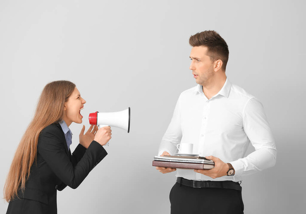 Businesswoman with megaphone shouting at her male secretary on light background - 写真・画像