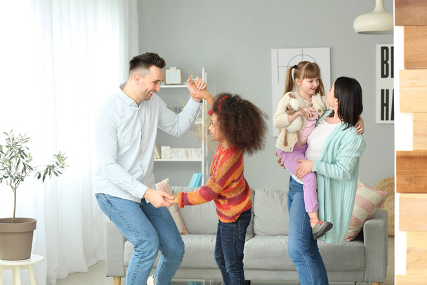 Ευτυχισμένο ζευγάρι με μικρά υιοθετημένα παιδιά που χορεύουν στο σπίτι - Φωτογραφία, εικόνα