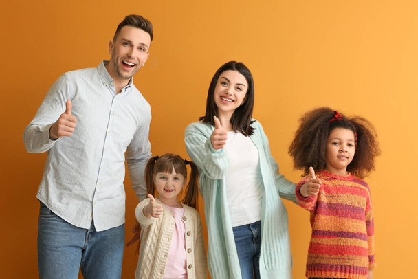 Счастливая пара с маленькими приемными детьми показывает большой палец вверх на цветном фоне
 - Фото, изображение