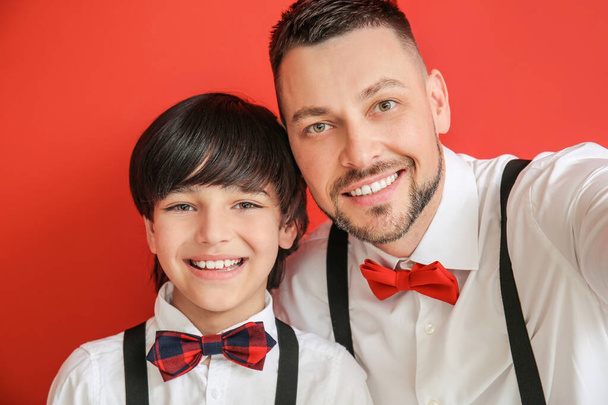 Stylish father and little son taking selfie on color background - Photo, Image