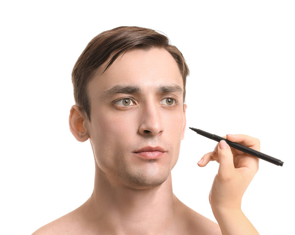 Plastic surgeon applying marking on man's face against white background - Photo, Image