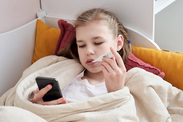 Enfermo adolescente acostado en la cama con termómetro usando el teléfono celular
 - Foto, imagen