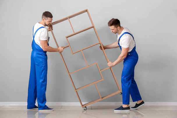 Cargadores que transportan muebles contra pared gris
 - Foto, Imagen
