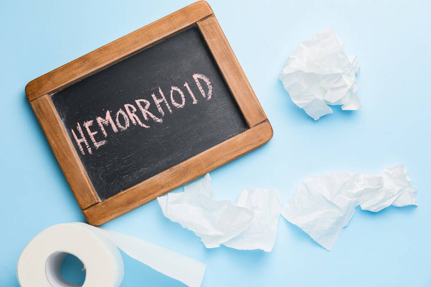 Papel higiênico e quadro com palavra HEMORRHOID sobre fundo de cor
 - Foto, Imagem