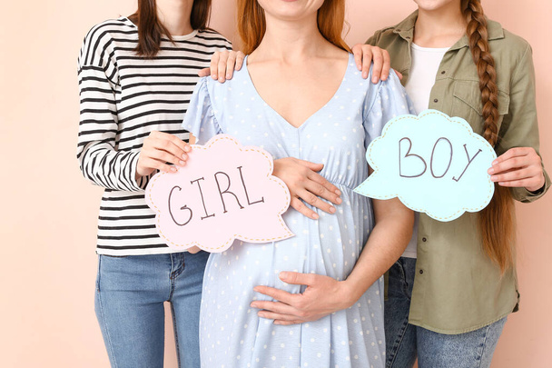 Lesbisch stel en zwangere vrouw met geschreven woorden GIRL en Boy op papieren tegen kleur achtergrond. Het concept draagmoederschap - Foto, afbeelding
