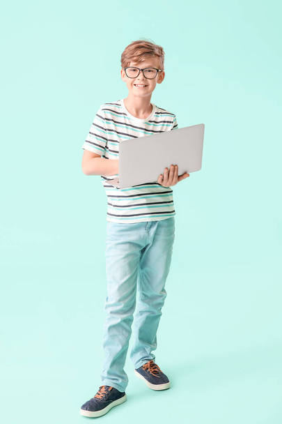 Cute little boy with laptop on color background. Concept of online education - Фото, изображение