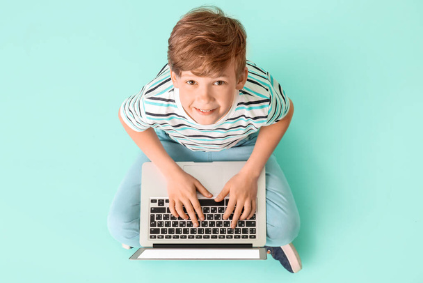 Cute little boy with laptop on color background. Concept of online education - Foto, Imagen