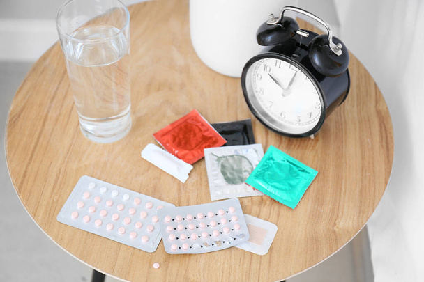 Различные средства контрацепции и часы на столе
 - Фото, изображение