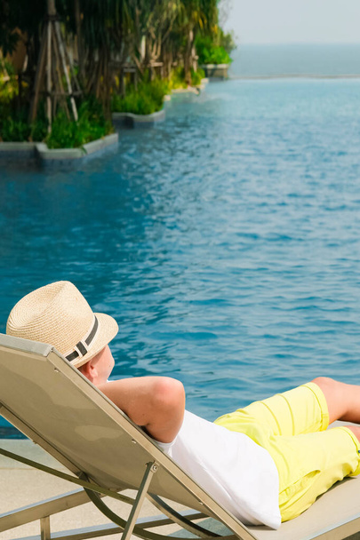 Boy on the longue chair near the swimming pool relaxing. Travel concept, travelling, hotel business. - Foto, imagen