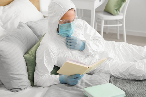 Man in biohazard suit reading book at home - Фото, изображение