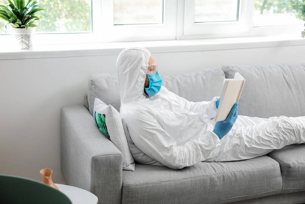 Man in biohazard suit reading book at home - Фото, зображення