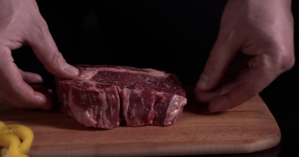 close-up χέρια μάγειρας ετοιμάζει κρέας για το μαγείρεμα σε μαύρο φόντο σε αργή κίνηση. Μοσχάρι σε ξύλινη σανίδα  - Πλάνα, βίντεο
