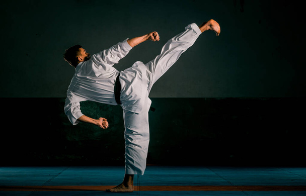 Молодой спортсмен в белом кимоно тренирует карате ката движется в спортзале - Фото, изображение