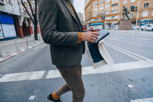 Jeune homme hipster moderne tenant un livre tout en marchant à travers la place de la ville
 - Photo, image