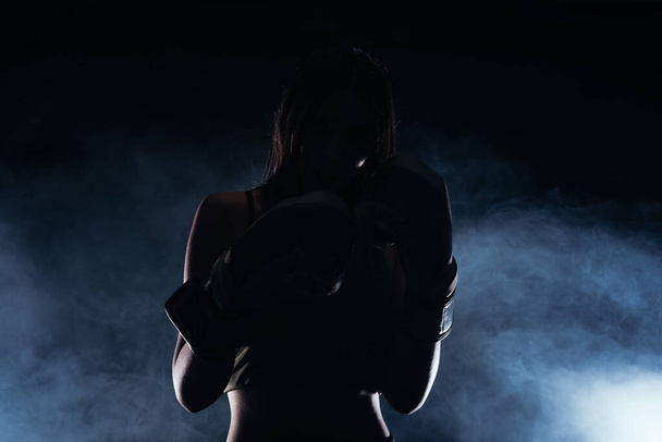 Silhouet portret met witte rook op de achtergrond van een vrouwelijk model met bokshandschoenen - Foto, afbeelding