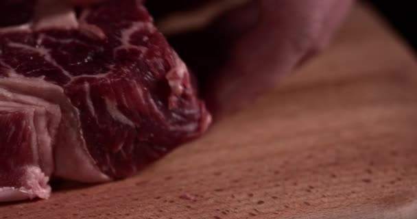 スローモーションで黒い背景に木製の板の上に生の牛肉。生ステーキ  - 映像、動画