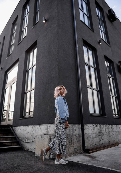una hermosa chica rubia en ropa informal urbana en el estilo de vida contra el fondo de una casa negra geométrica - Foto, imagen