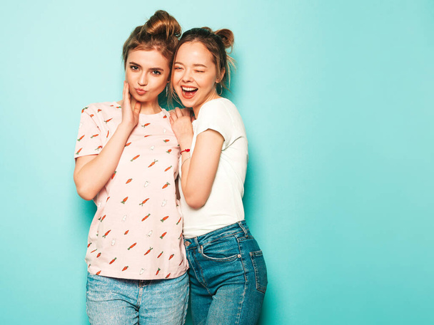 Two young beautiful blond smiling hipster girls in trendy summer hipster jeans clothes. Sexy carefree women posing near blue wall. Trendy and positive models having fun - Φωτογραφία, εικόνα