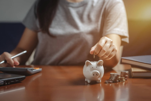 Weibliche Hand legt Geld in Sparschwein, um Geld zu sparen, schreiben Finanzen. - Foto, Bild