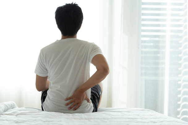 Aasialainen mies selkäkipu ja istua sängyssä makuuhuoneessa aamulla - Valokuva, kuva