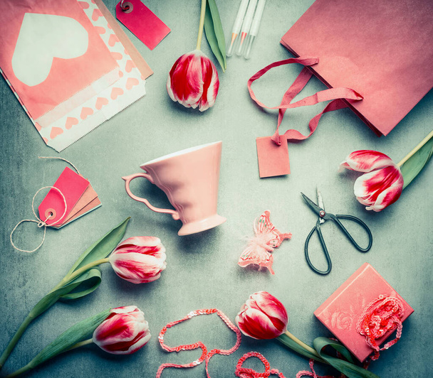Still life with tulips, pink cup, shopping bag, gift box, shear and paper envelope with heart, top view, Flat lay styling. Mothers Day greeting concept - Photo, Image