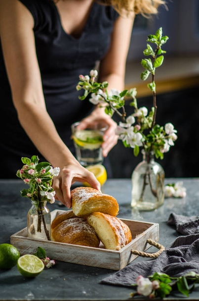 Woman preparing breakfast with croissants and lemonade. Spring flowers on the table. - Fotó, kép
