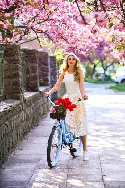 Spring style travel. retro woman sell tulip flower bouquet. girl under sakura with vintage bicycle. spring beauty and fashion. cherry tree pink blossom. perfect smell. perfume spa and allergic - Фото, изображение