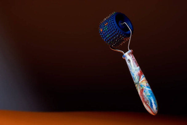 Massager with blue drum, plastic multicolored handle and metal needles on dark background. Subject and promotional photography. For relaxation and health. - Photo, Image